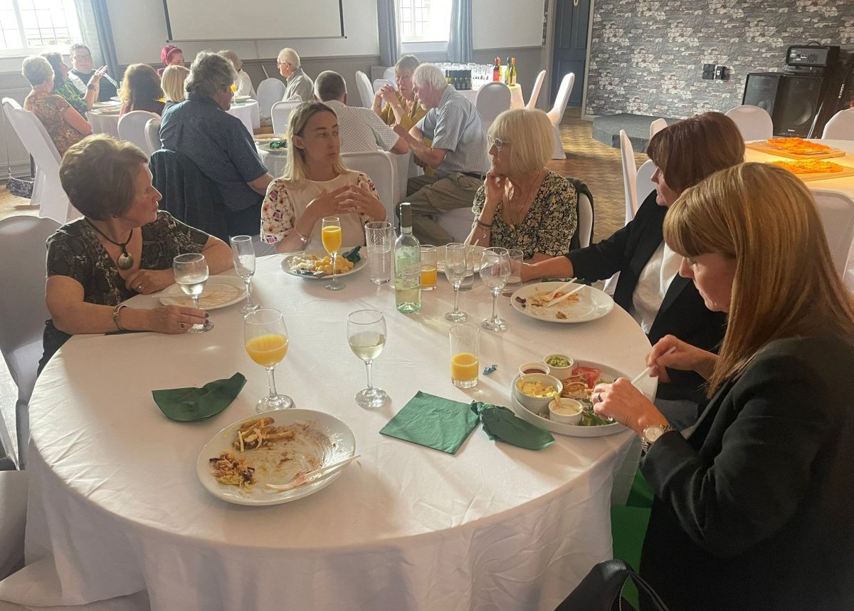 women at a celebration lunch sat around round table eating food