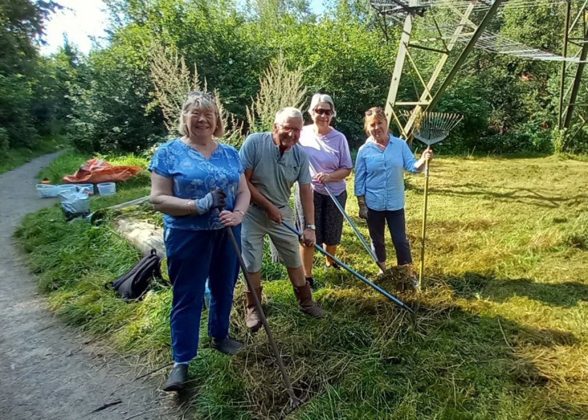 group of men and women smiling with gardening tools in communal green area