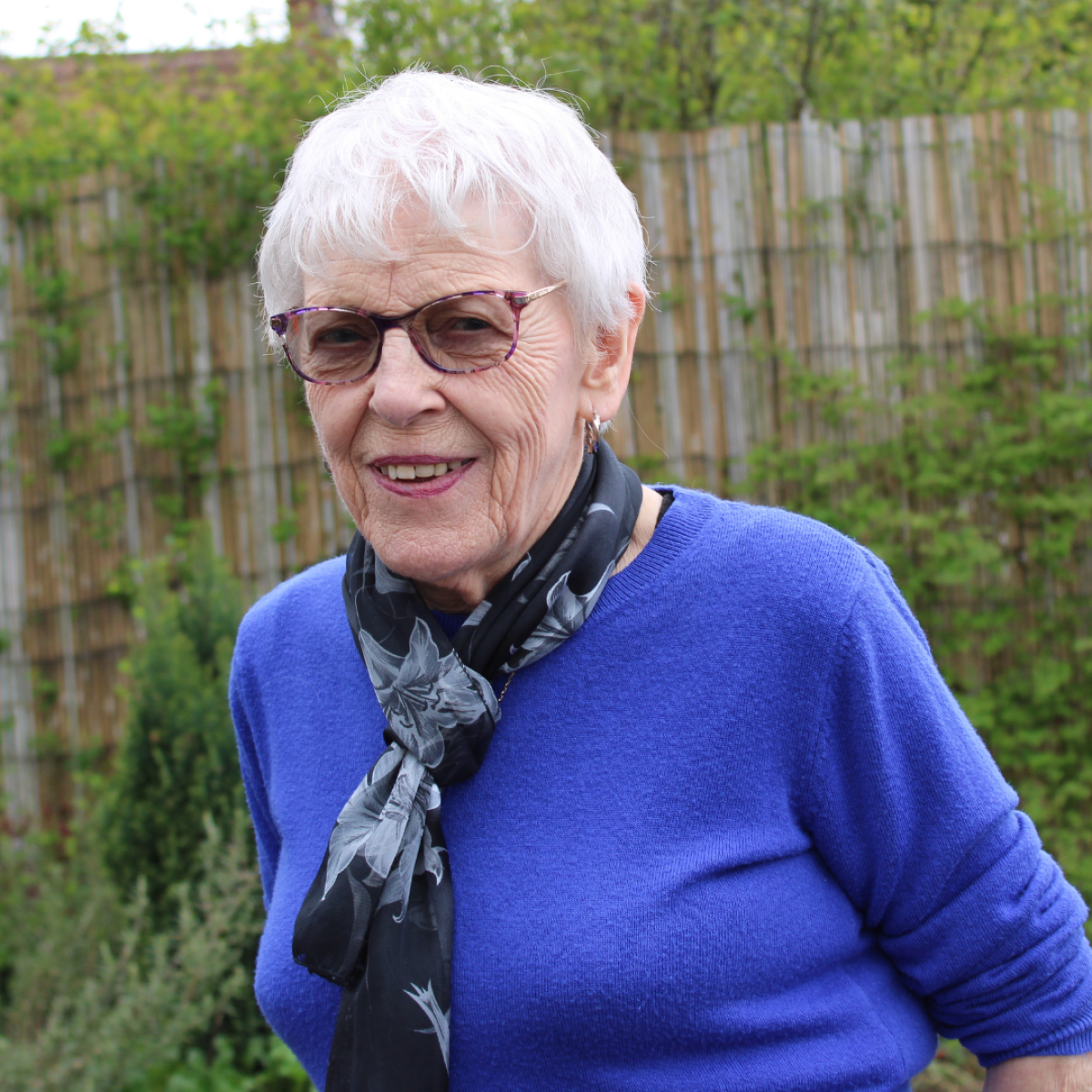 photo of a woman in blue jumper and floral scarf with white hair and glasses