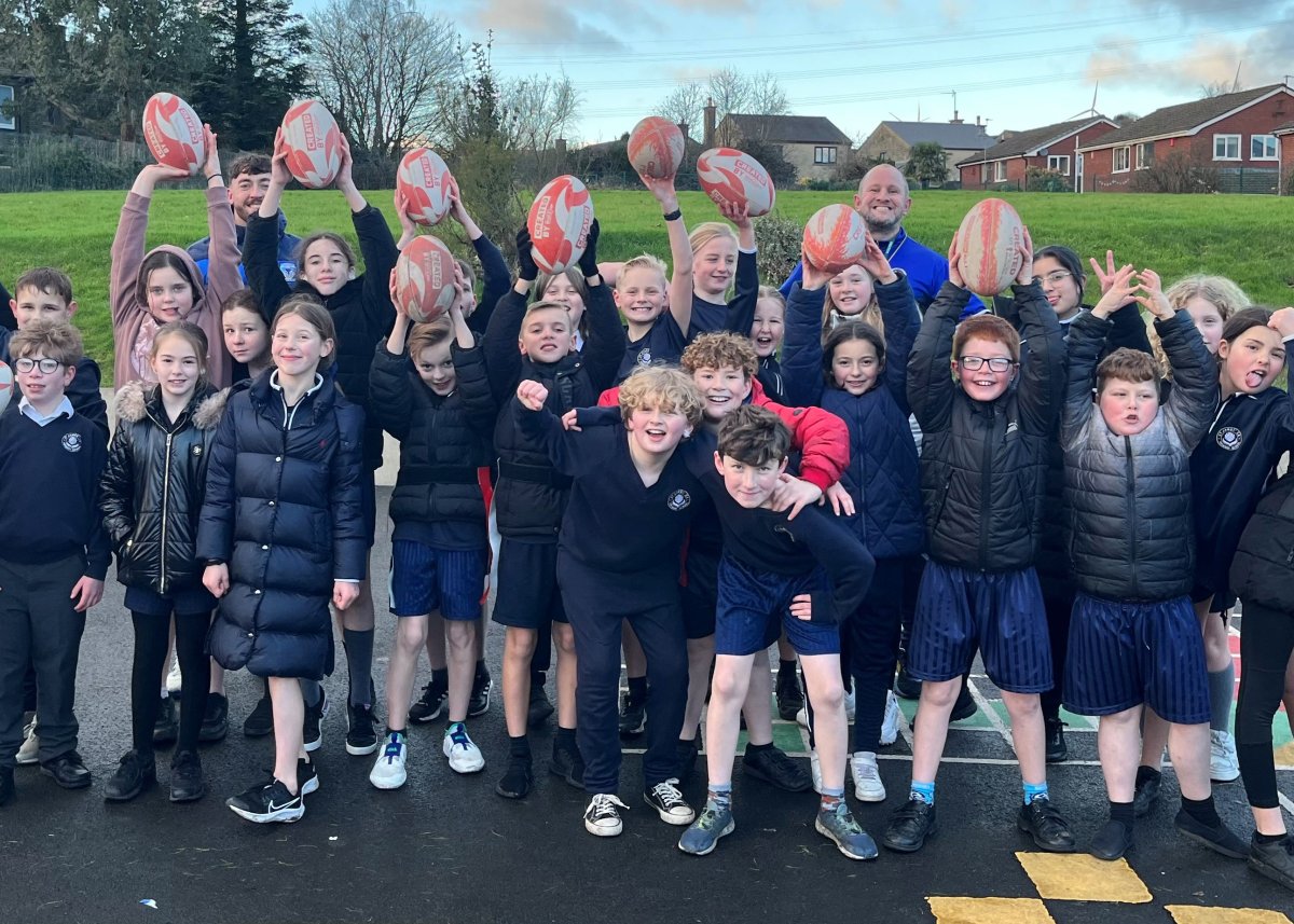 group of children holing rugby balls in the air and cheering