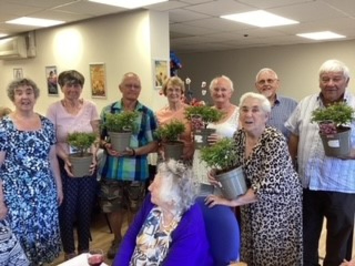 older people's group smiling holding gift plant pots