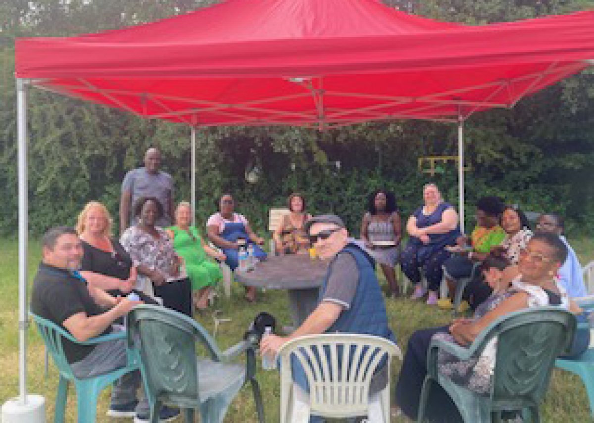 group of people sat in circle on garden chairs at a barbecue under gazebo