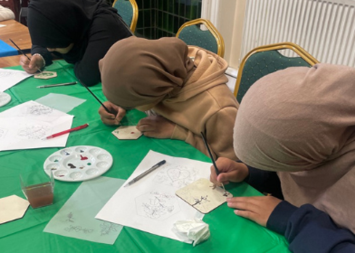 girls wearing headscarves writing and drawing at table