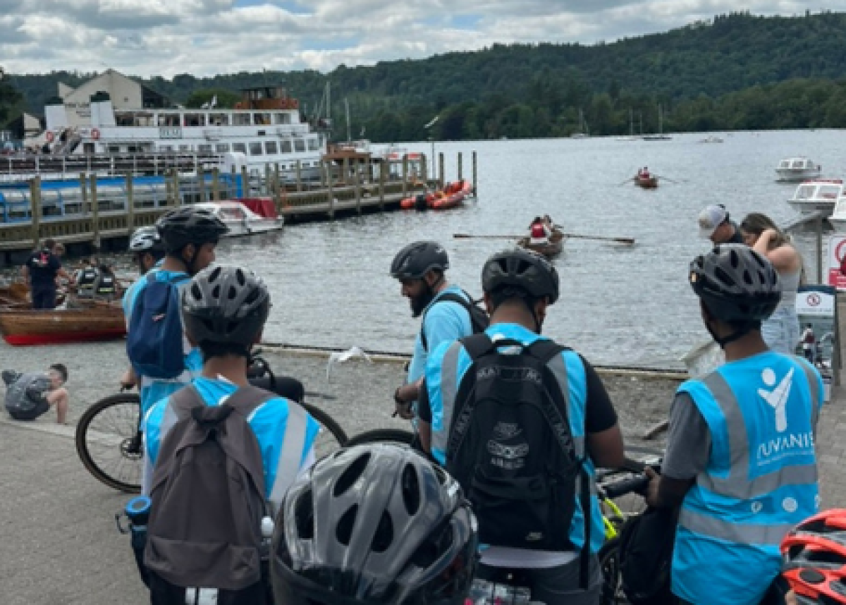 group of cyclists wearing helmets overlooking lake with passenger boat on it